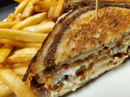 A close-up of a crispy grilled sandwich with coleslaw, served with a side of golden French fries.