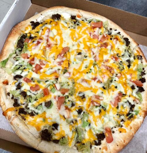 A pizza topped with ground beef, shredded cheese, lettuce, and diced tomatoes on a golden crust.