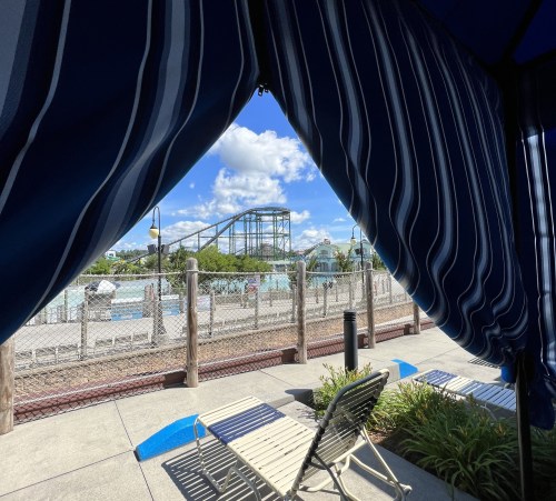 View of a water park with a roller coaster in the background, seen through a striped cabana curtain.