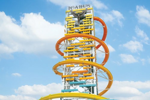 A tall water slide tower with colorful spirals against a blue sky with clouds. The slide is named "Icarus."