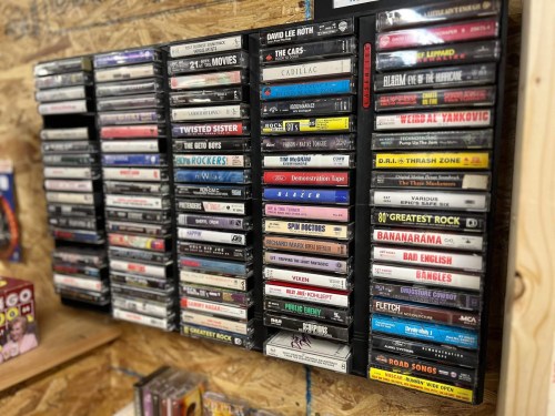 A wall display of various cassette tapes organized in cases, featuring titles from different music genres and artists.