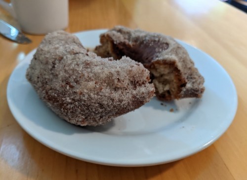 A plate with two sugar-coated donuts, one partially bitten, on a wooden table.