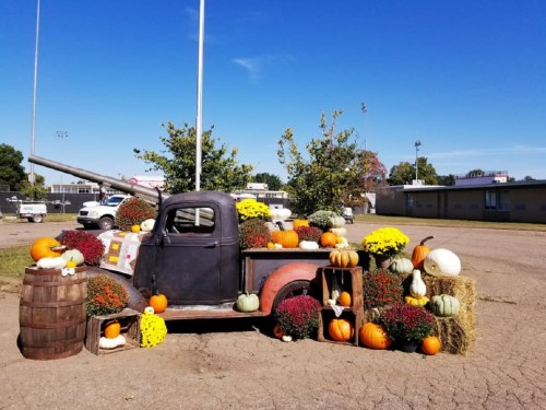 A vintage truck surrounded by colorful pumpkins and mums, set against a clear blue sky.
