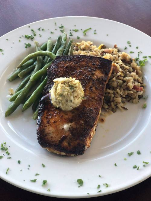 Grilled salmon fillet topped with herb butter, served with green beans and a side of rice pilaf.