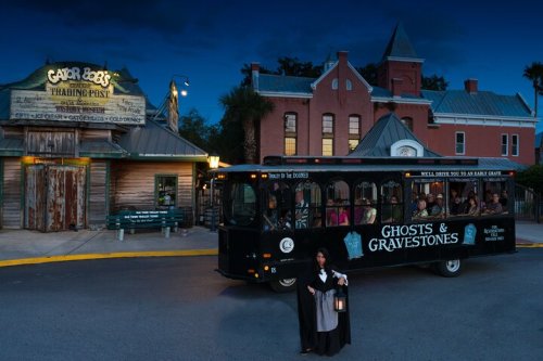 A ghost tour trolley parked outside Gator Bob's Trading Post at dusk, with a guide holding a lantern in front.