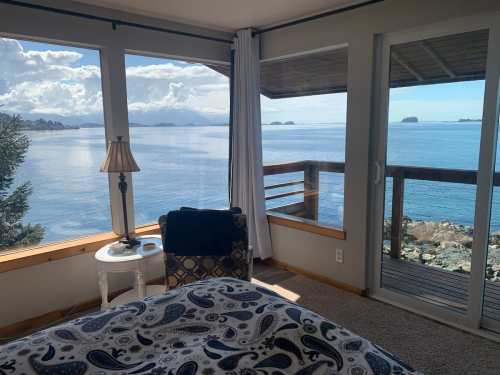 Cozy bedroom with a view of the ocean and islands, featuring a lamp, chair, and large windows letting in natural light.
