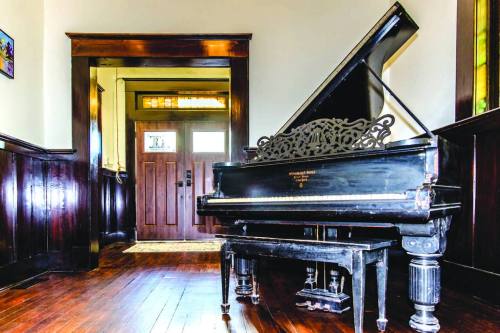 A grand piano in a warmly lit entryway with wooden walls and a front door visible in the background.