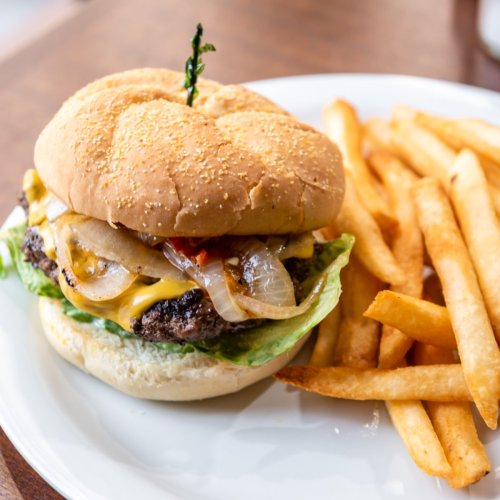 A juicy cheeseburger with lettuce, onions, and a slice of tomato, served with a side of golden French fries.