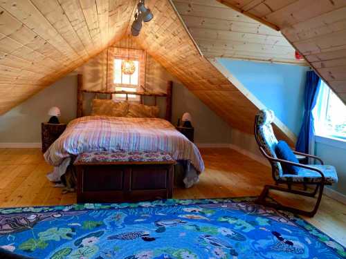Cozy attic bedroom with a sloped ceiling, wooden accents, a bed, rocking chair, and colorful rug.