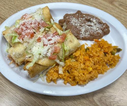A plate of crispy taquitos topped with lettuce, tomato, and cheese, served with rice and refried beans.