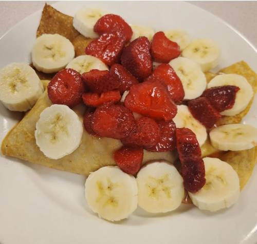 A plate of crepes topped with sliced bananas and fresh strawberries.