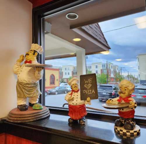 Three cheerful chef figurines stand on a windowsill, one holding a pizza, another a sign that says "WE ❤️ PIZZA."