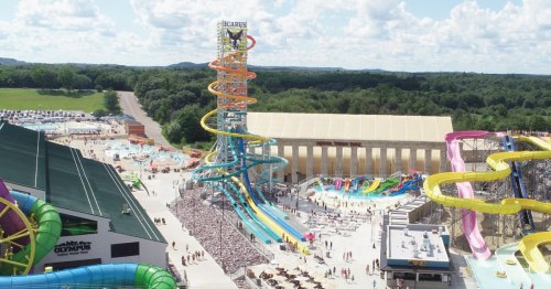Aerial view of a water park featuring colorful slides, a tall water tower, and a large crowd enjoying the attractions.