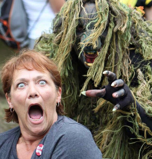 A surprised woman gasps as a creature covered in moss and branches reaches toward her from behind.