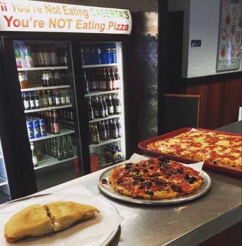 A display of pizzas at a pizzeria, with a sign reading "If You're Not Eating Caserta's, You're NOT Eating Pizza."