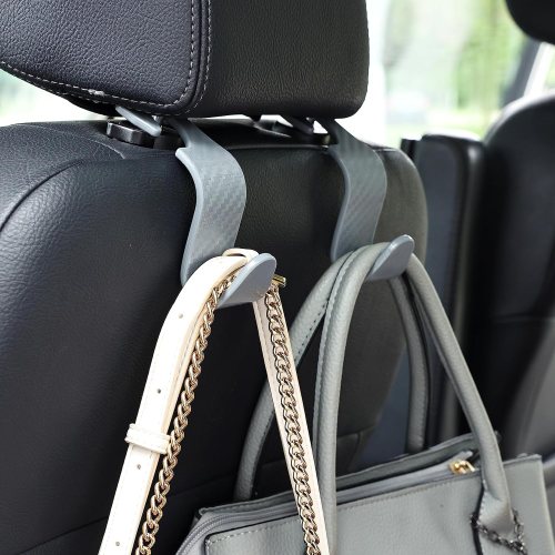 A handbag hanging from a car seat headrest, secured with a strap, against a backdrop of the car interior.