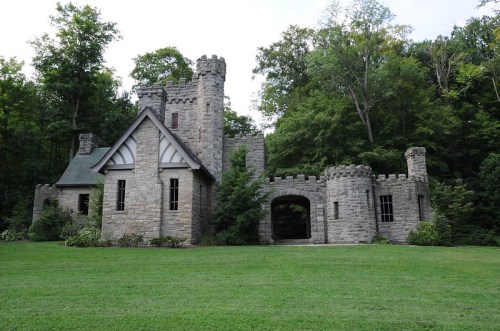 A stone castle with towers surrounded by trees and a grassy lawn.