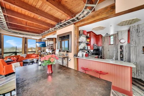 Modern open-concept living space with a kitchen, dining area, and cozy seating, featuring large windows and vibrant decor.