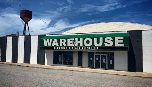 Exterior of a vintage emporium named "Warehouse" with a water tower in the background and a blue sky.