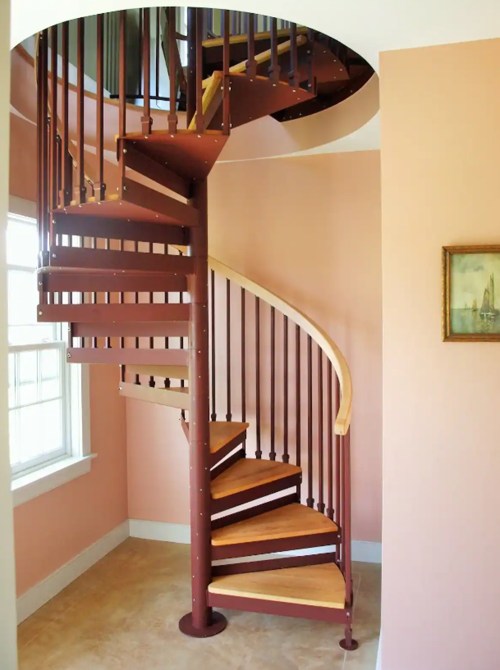 A modern spiral staircase with wooden steps and a metal frame, set against a peach-colored wall.