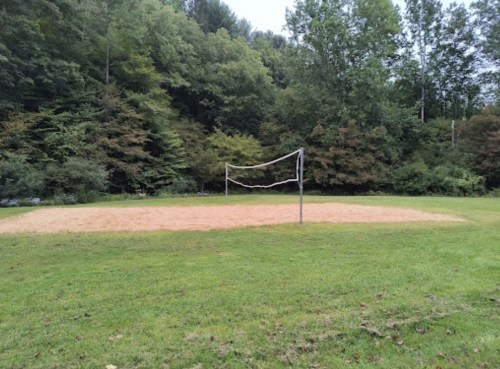A sandy volleyball court with a net, surrounded by green grass and trees in the background.