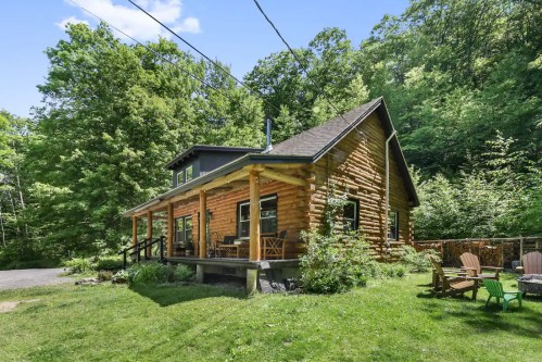 A charming log cabin surrounded by lush greenery, featuring a porch and outdoor seating.