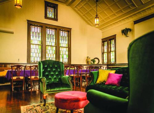 Cozy interior featuring green armchairs, a pink ottoman, and stained glass windows in a warm, inviting space.