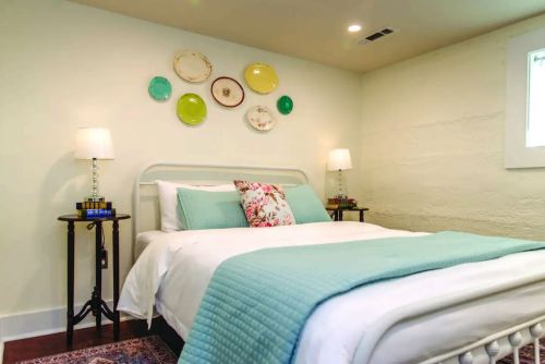 Cozy bedroom with a white bed, decorative plates on the wall, and bedside tables with lamps. Soft blue accents.