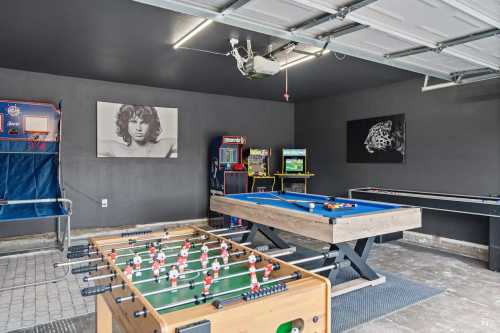 A garage game room featuring a foosball table, pool table, arcade games, and wall art.