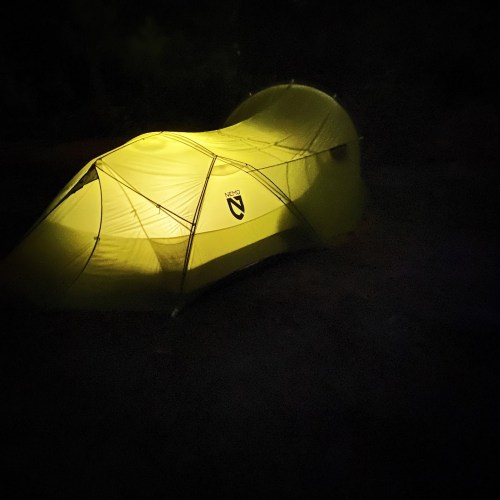 A glowing yellow tent illuminated in the dark, set against a nighttime background.