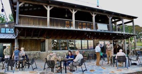 A rustic building with outdoor seating, where people gather and socialize on a stone patio during sunset.