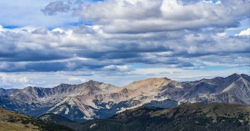 A panoramic view of rugged mountains under a cloudy sky, showcasing peaks and valleys in a natural landscape.