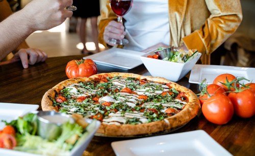 A table set with a large pizza topped with tomatoes and basil, surrounded by fresh tomatoes and salad.