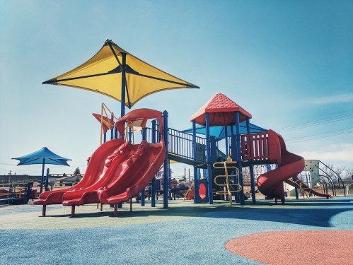 Colorful playground with red slides, climbing structures, and yellow shade canopies under a clear blue sky.