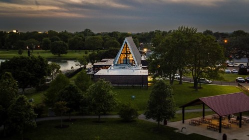 Aerial view of a modern triangular building surrounded by trees and a park at dusk.