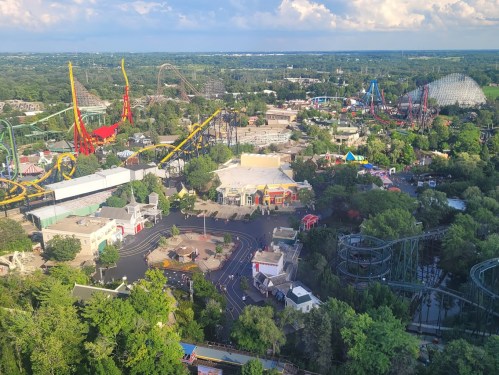 Aerial view of an amusement park featuring roller coasters, rides, and lush greenery under a partly cloudy sky.
