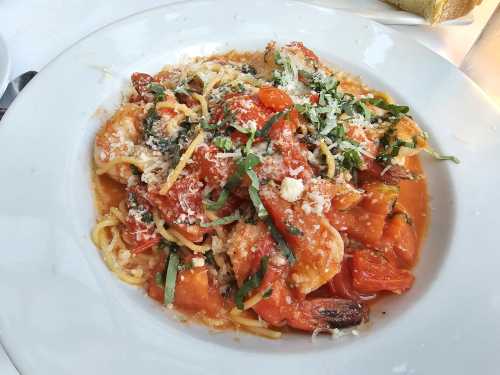 A plate of pasta with shrimp, tomatoes, basil, and grated cheese in a rich tomato sauce.