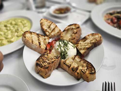 A plate with grilled bread arranged in a flower shape, topped with fresh tomatoes and a creamy burrata cheese.