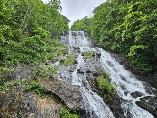A cascading waterfall flows down a rocky cliff, surrounded by lush green trees and foliage.