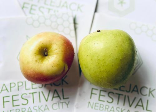 Two apples, one red and one green, placed on top of festival flyers for the Appljack Festival in Nebraska City.