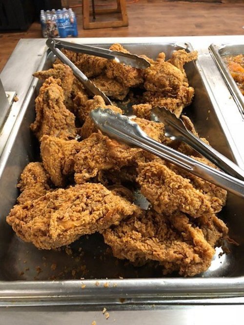 A metal tray filled with crispy fried chicken pieces, with tongs resting on top.