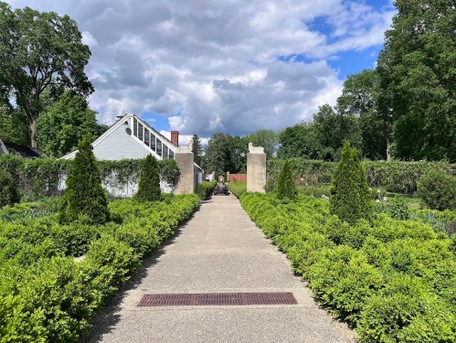 A pathway lined with greenery leads to a building under a partly cloudy sky.