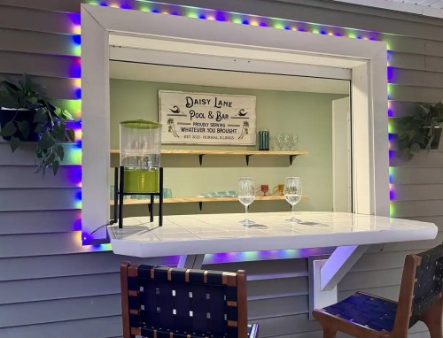 A bar window with colorful lights, featuring a drink dispenser and two glasses, set against a cozy interior backdrop.