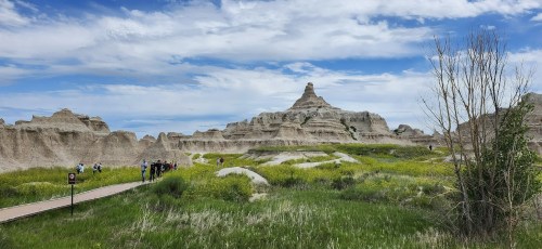 A scenic view of rugged rock formations and green grass, with a group of people walking along a path under a blue sky.