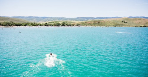 A person rides a jet ski toward a busy beach and over bright blue water at Bear Lake Utah.