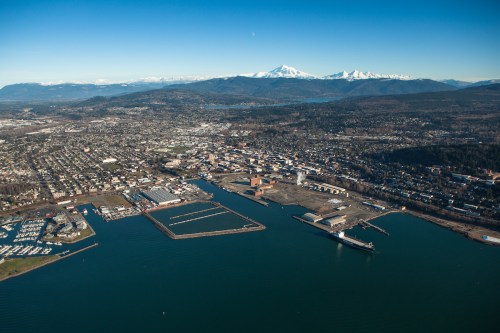 Aerial view of a coastal city with a harbor, mountains in the background, and clear blue skies.