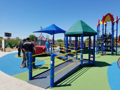 A colorful playground with various structures and people enjoying the space on a sunny day.