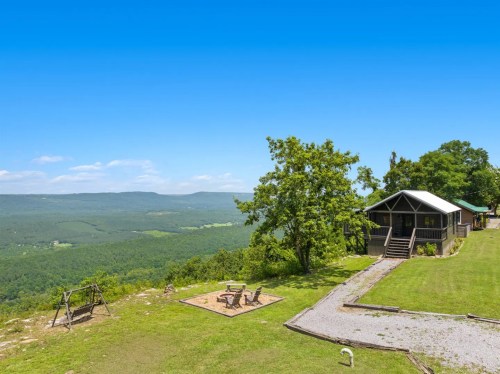 A scenic view of a green valley from a hillside cabin, featuring a swing set and fire pit in the foreground.