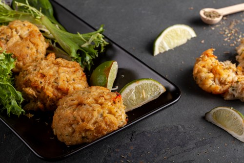 Plate of golden crab cakes with lime wedges and fresh greens on a dark surface.