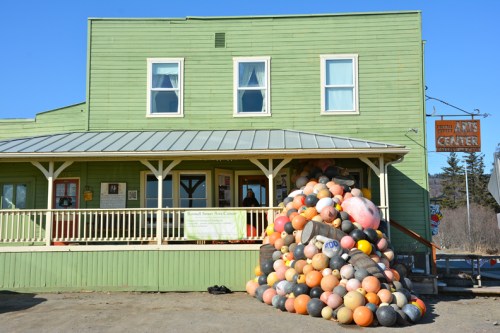 A colorful pile of buoys in front of a green building with a sign for an arts center.